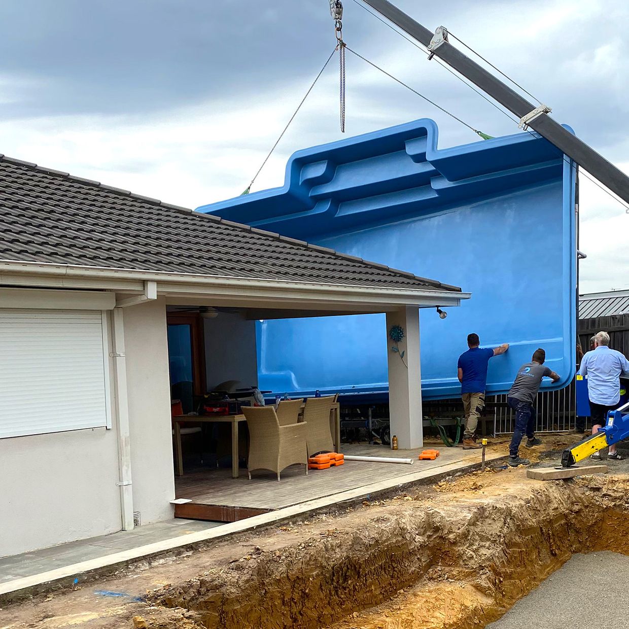 Fibreglass pool shell being craned beside a house