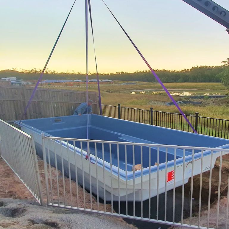 Fibreglass pool shell being craned over a fence